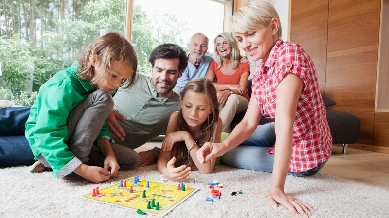 Rodina s různými generacemi sedí na podlaze a hrají deskovou hru "Člověče, nezlob se" v obývacím pokoji.