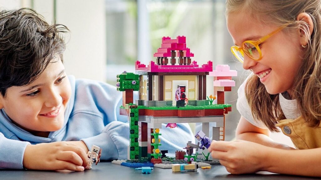 Dvě děti, chlapec a dívka, se usmívají, zatímco si společně hrají s barevným Lego Minecraft setem na stole.