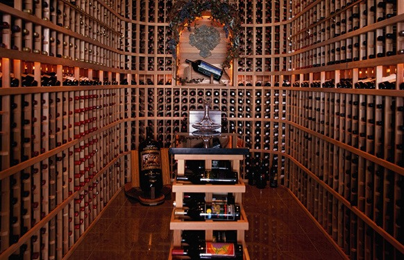 Elegantní vinotéka s obrovskou sbírkou láhví vína uspořádaných do vysokých dřevěných regálů v útulné místnosti s bohatou dekorací a vínovou tematikou.