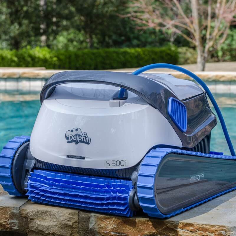 Robotický vysavač značky Dolphin model S300i, stojící na okraji bazénu, s modrými kartáči a pružnou modrou hadicí.
