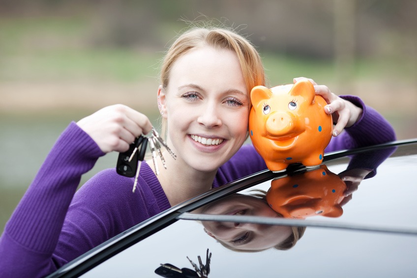 Šťastná mladá žena ukazuje klíče od auta a drží prasátko na kapotě auta, symbolizující úspory na povinném ručení.