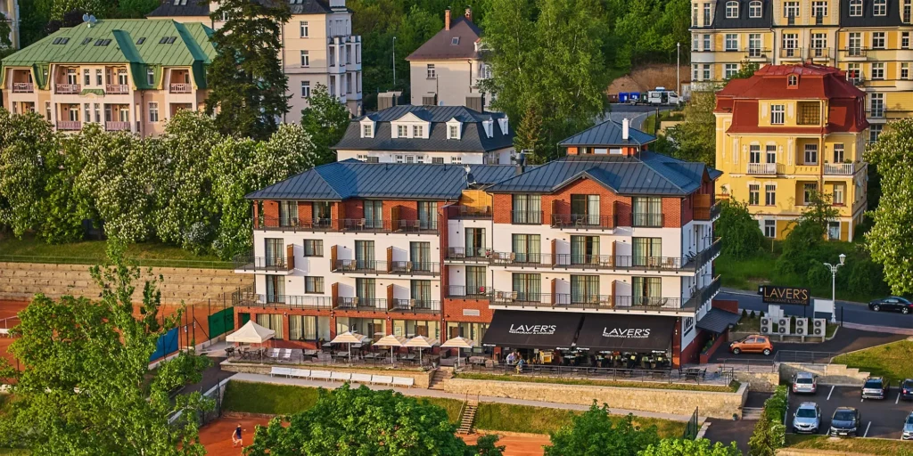 Hotel & Wellness Queens v Mariánských Lázních – moderní čtyřhvězdičkový hotel s prostornými balkony, restaurací Laver’s a tenisovými kurty v malebném lázeňském prostředí obklopeném historickými budovami a zelení.
