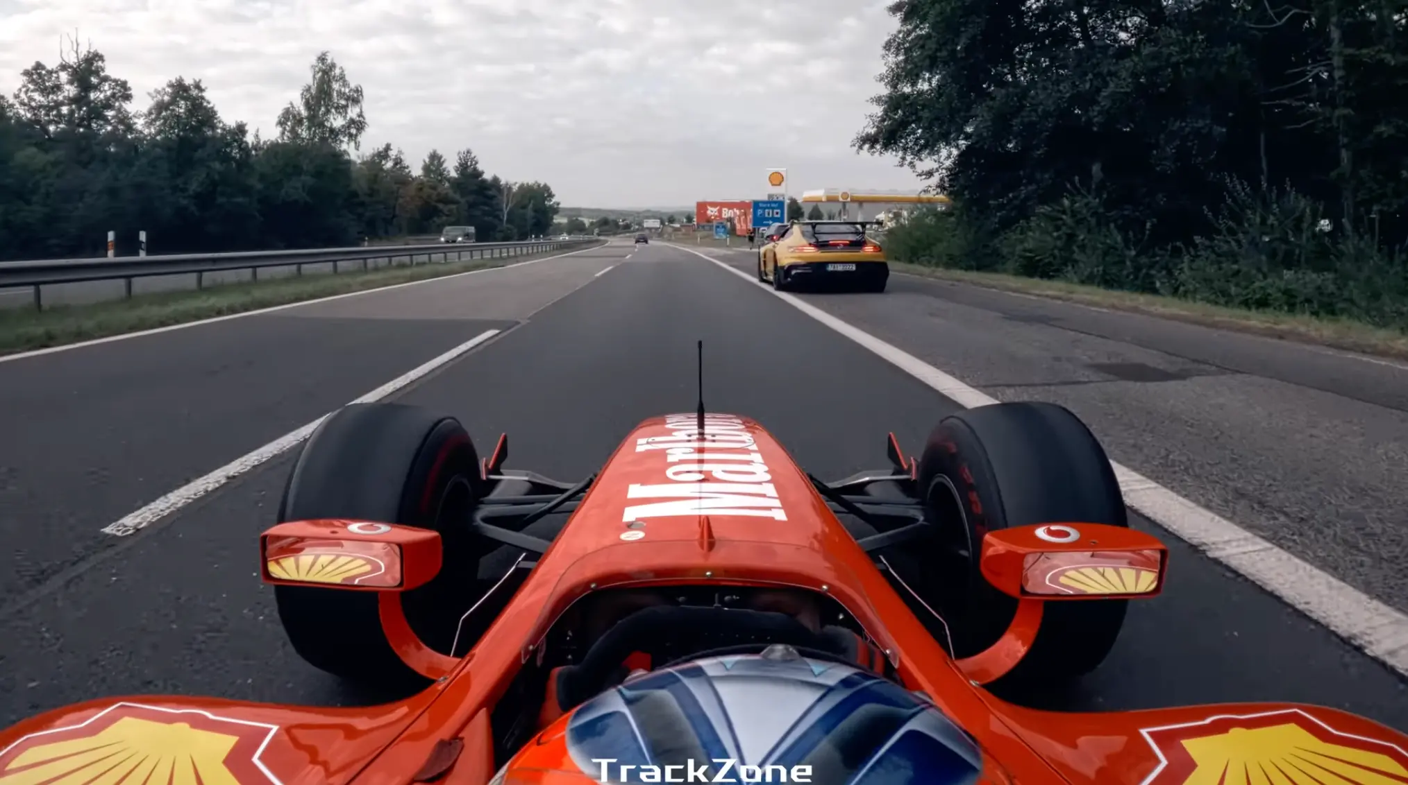 Záběr z kokpitu formule jedoucí po dálnici D4, před vozem žlutý sportovní automobil – akční jízda mimo závodní okruh.