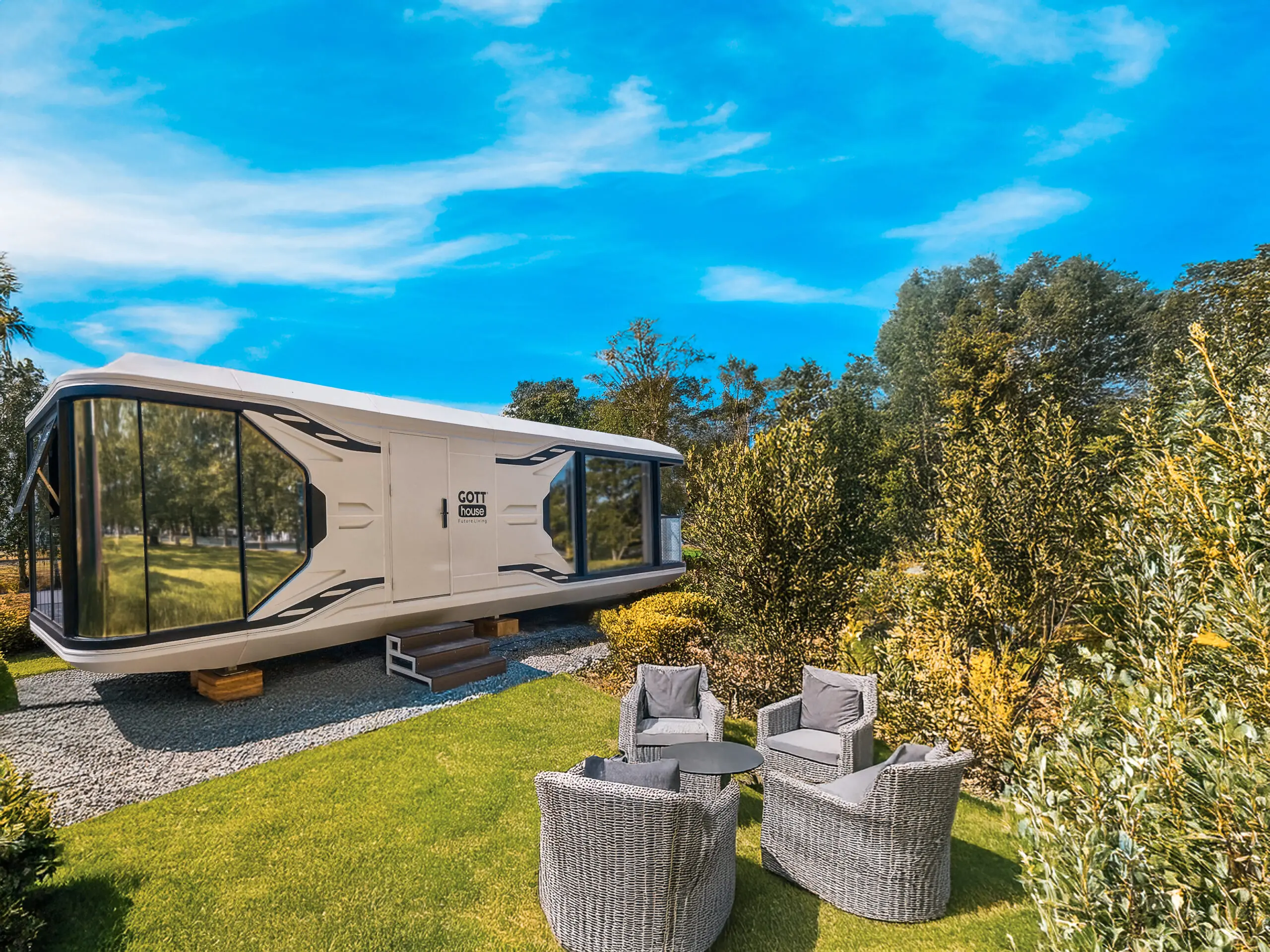 Mobilní dům GOTThouse umístěný v zahradě za slunečného dne, s venkovním posezením a okolní zelení