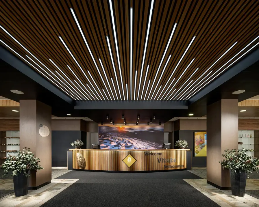 Moderní recepce čtyřhvězdičkového Pinia Hotel & Resort ve Špindlerově Mlýně s elegantním dřevěným stropem a atmosférickým podsvícením.