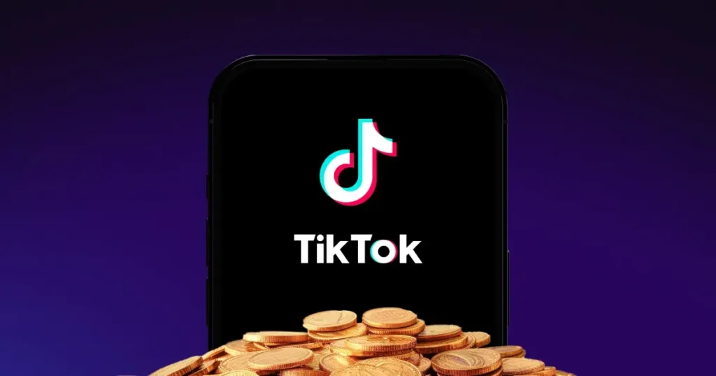 Telefon s logem TikToku a hromadou zlatých mincí v popředí – symbol vydělávání peněz přes tuto sociální síť.