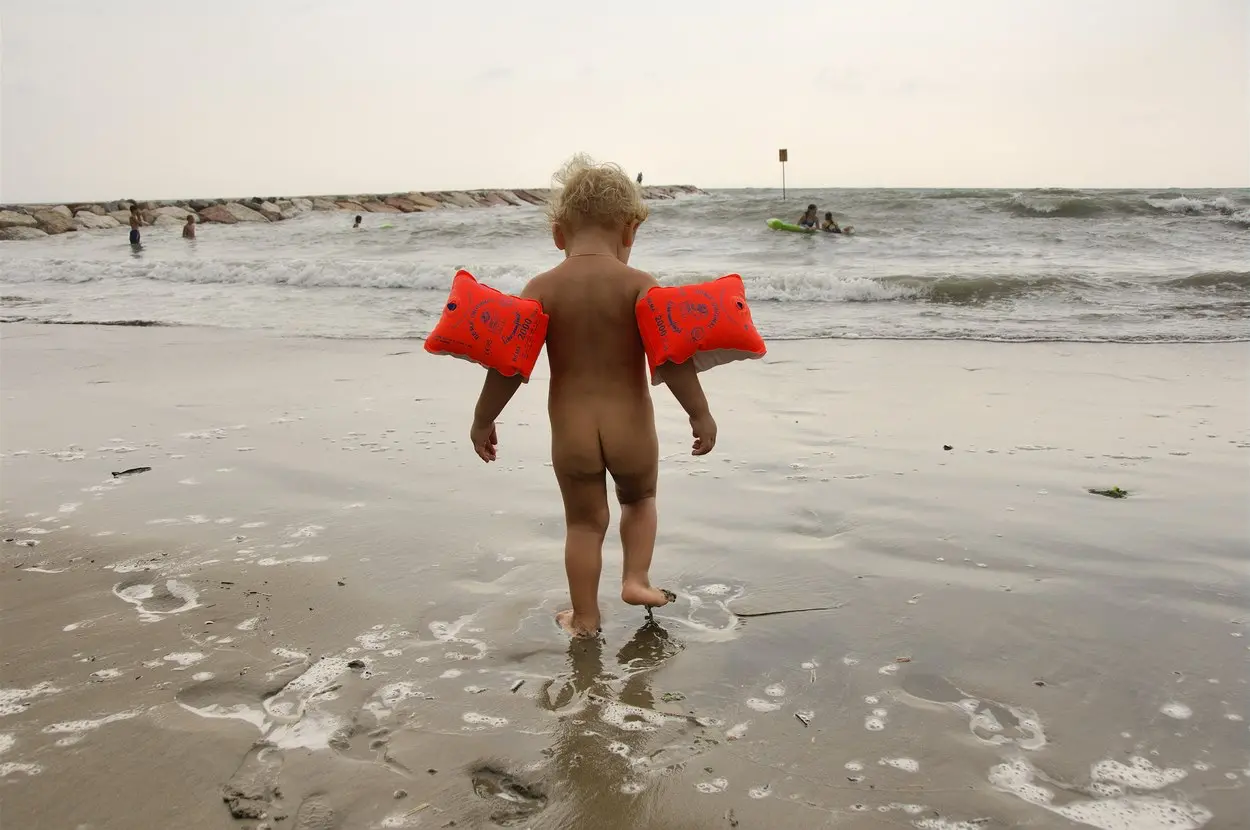 Malé dítě na pláži jen s rukávky – ukázka, proč by rodiče neměli dávat nahaté fotky dětí na internet.