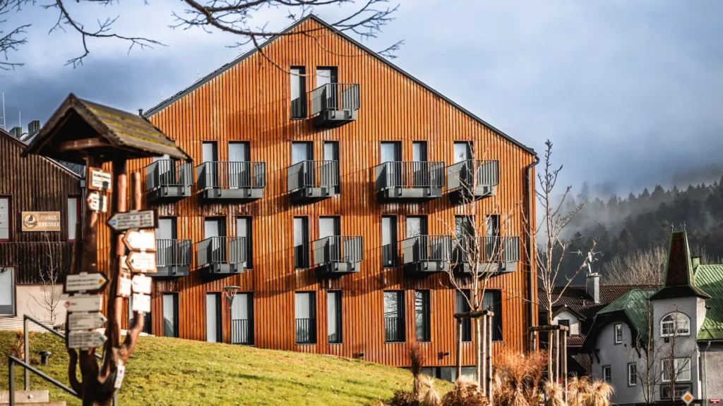 Moderní dřevěný wellness hotel na Šumavě s balkony a mlhavým lesem v pozadí