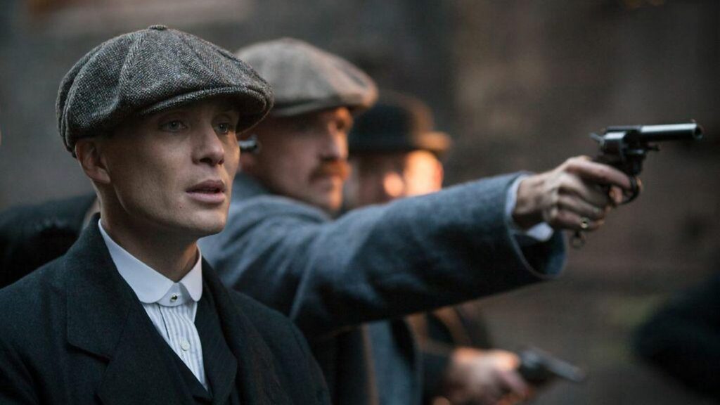 Thomas Shelby s čepicí a zbraní během dramatické scény ze seriálu Peaky Blinders