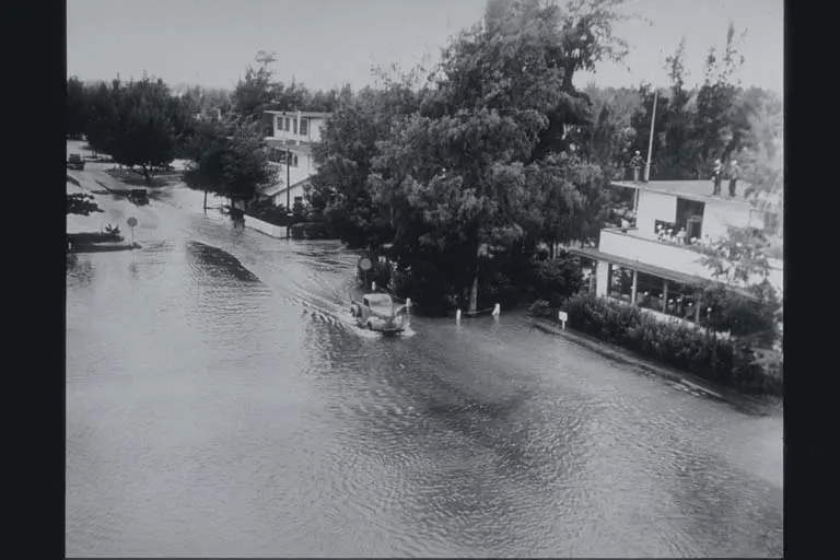Ulice zaplavené vodou po zemětřesení. Staré auto si razí cestu skrz město, kde je voda až po nárazník.