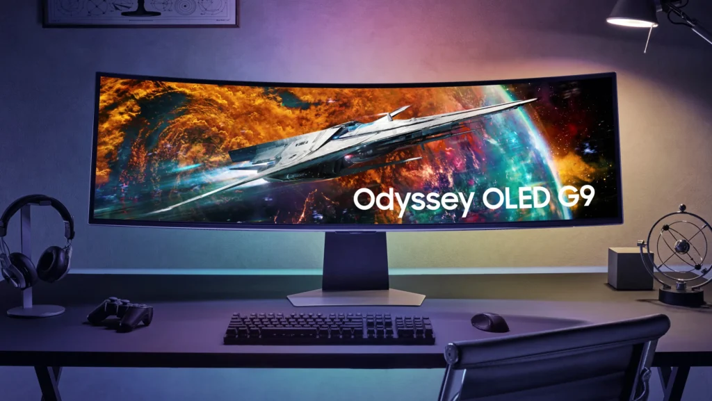Ultrawide herní monitor Samsung Odyssey OLED G9 na herním stole s klávesnicí, ovladačem a sluchátky v moderním herním setupu.