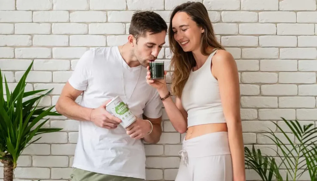 Mladý pár ochutnává zelený nápoj Blendea Supergreens u zdi z bílých cihel