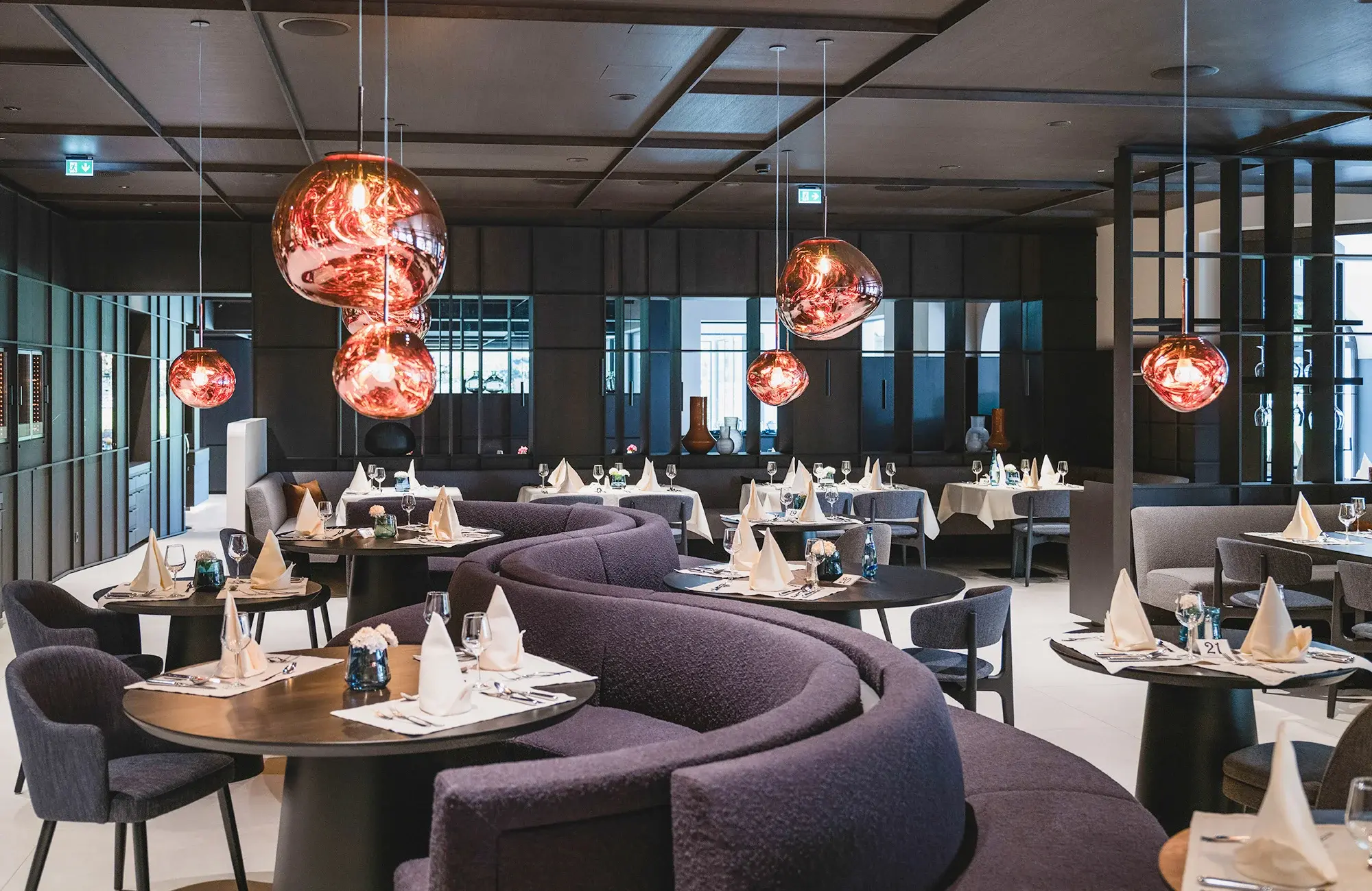 Moderní restaurace v Neuhaus Zillertal Resortu v Mayrhofenu s elegantním interiérem, stylovým osvětlením a připravenými stoly na večeři.