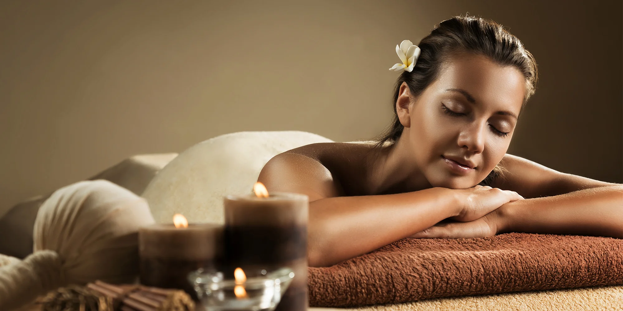 Usměvavá žena odpočívá na masážním lehátku, obklopená svíčkami a klidem
