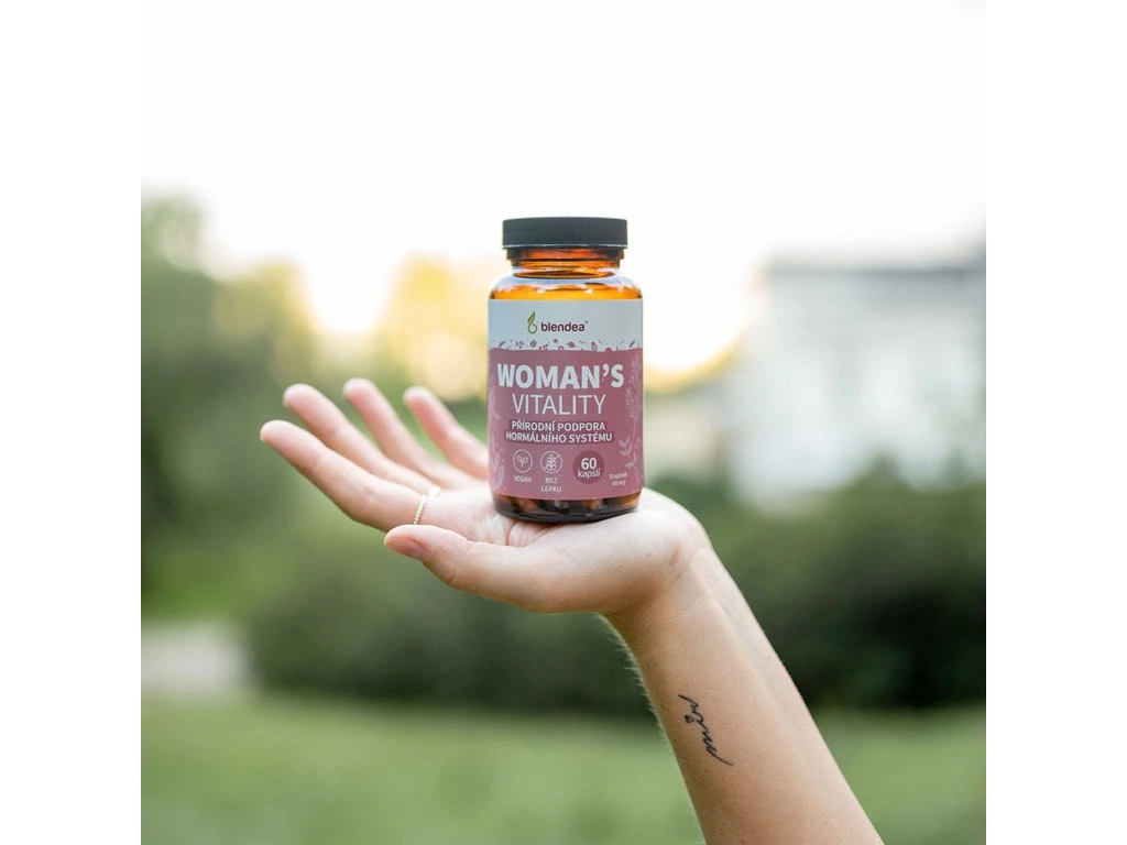 336-3_woman-s-vitality-60-kapsli | Venclíkovi.cz Blendea Woman’s Vitality v elegantní skleněné lahvičce, držená v ženské ruce na pozadí přírody.