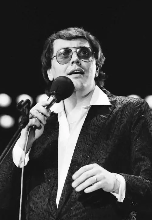 Karol Duchoň zpívající na koncertě v elegantním saku a brýlích