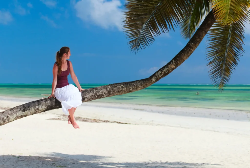 Dívka sedící na palmě u pláže v Keni - klid, tropy a ten pravý únik ze zimy