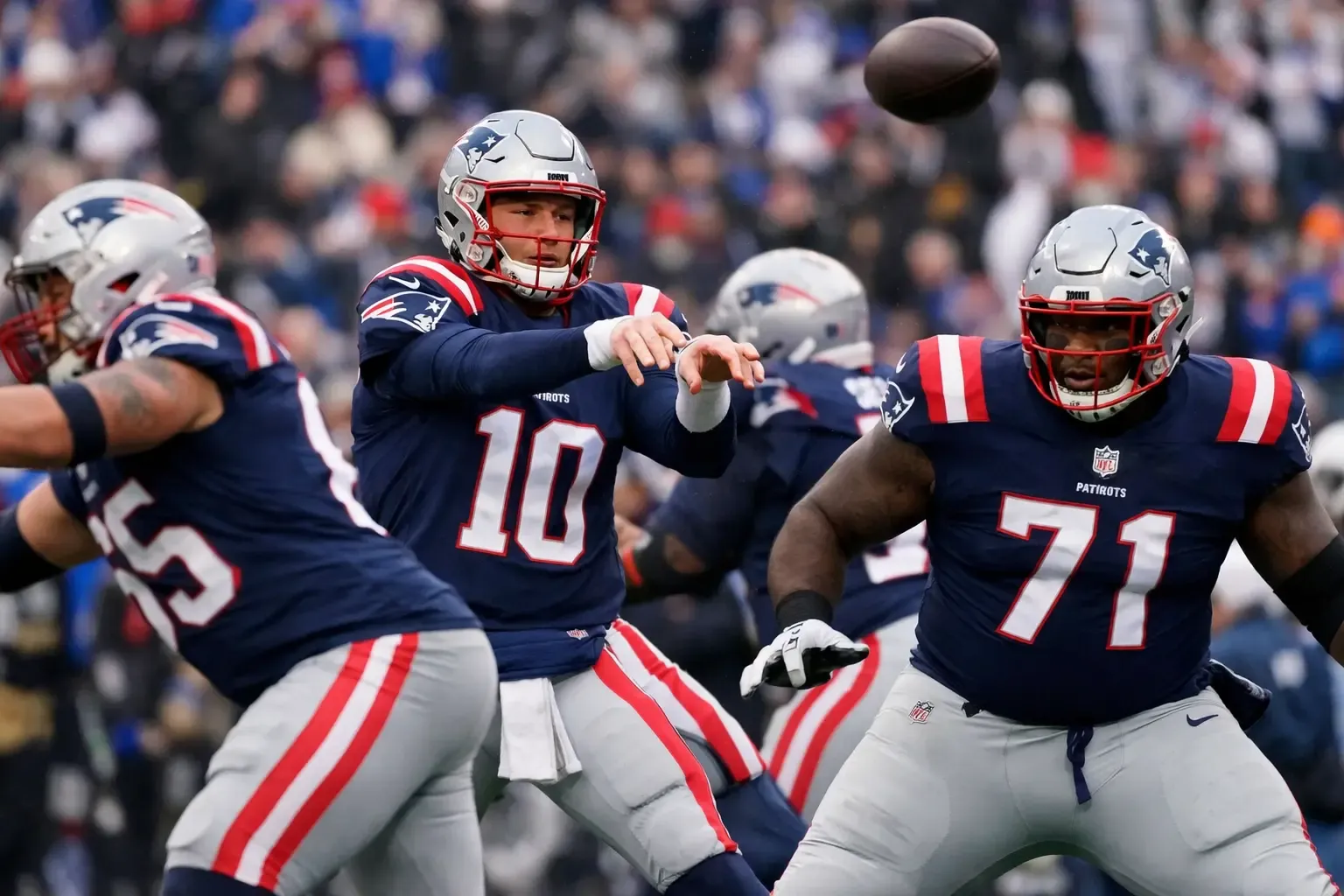 prihravka-patriots | Venclíkovi.cz Quarterback Patriots Drake Maye při přihrávce během zápasu, chráněný ofenzivní linií s čísly 65 a 71.