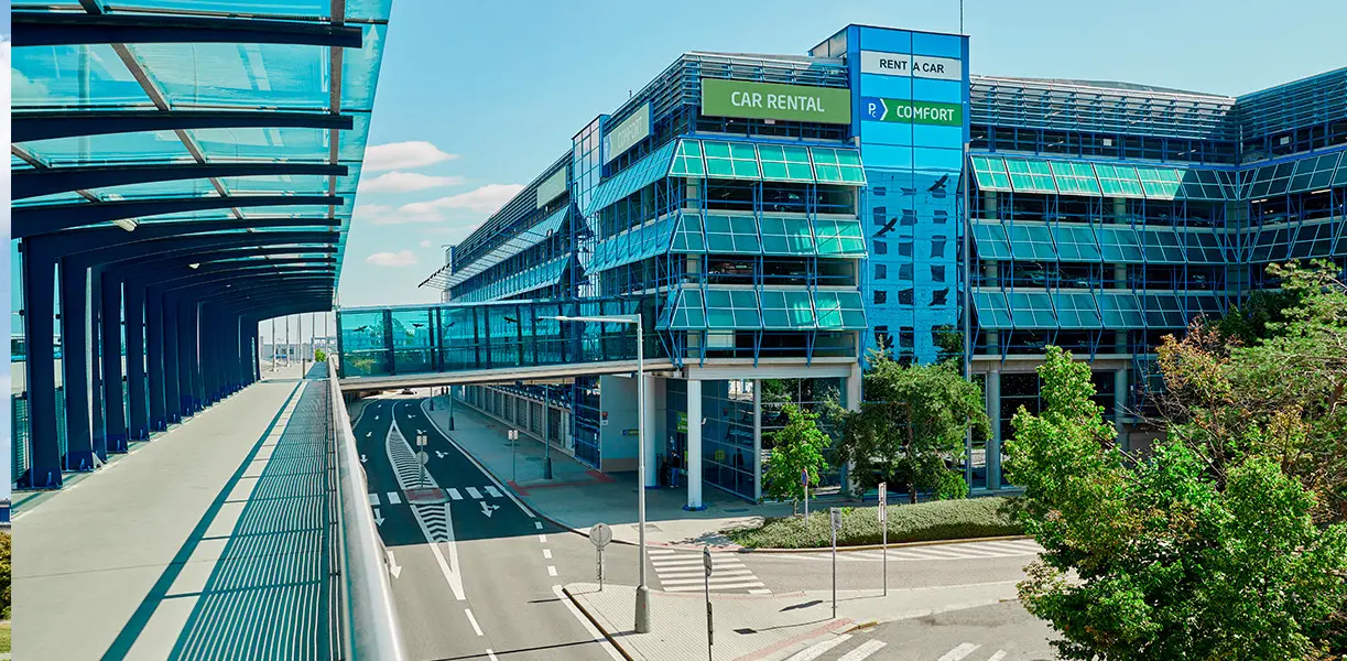 Oficiální domy PC Comfort _ PA Smart | Venclíkovi.cz Moderní modře prosklená budova parkovacího domu PC Comfort na letišti Praha s nadzemním proskleným koridorem pro pěší.