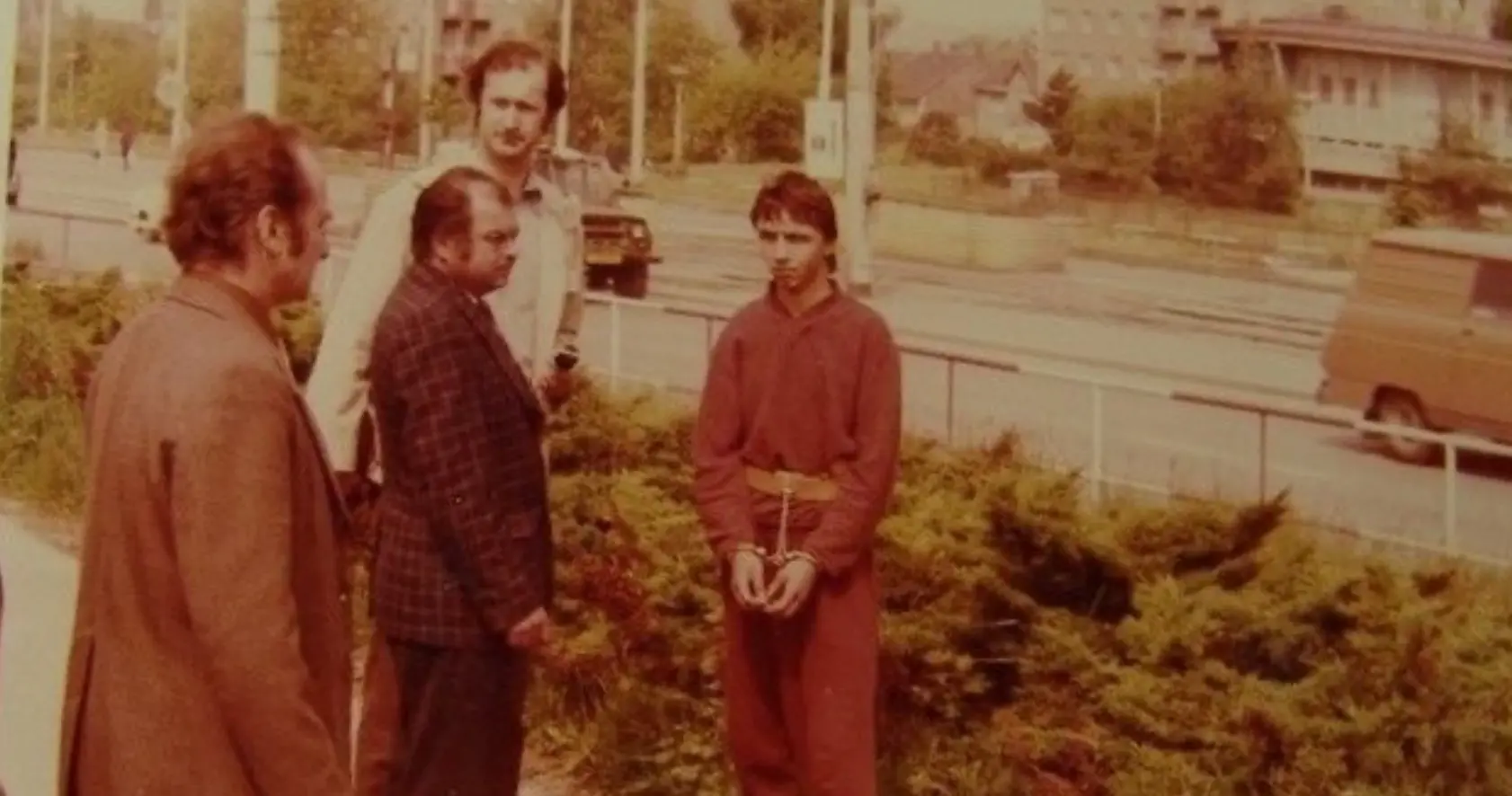 Spartakiádní vrah Straka - dobová foto 2 | Venclíkovi.cz Jiří Straka v červeném vězeňském úboru a s pouty na rukou stojí u velkých odpadních kontejnerů během vyšetřování.