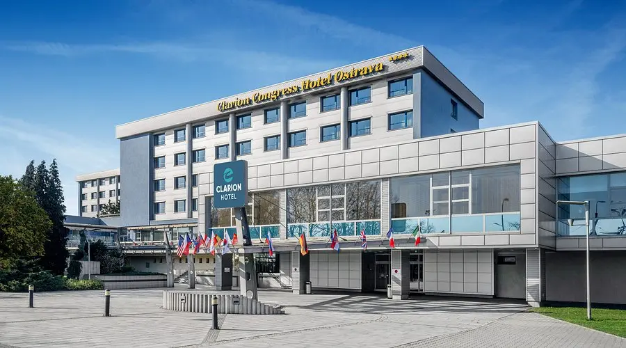 clarion Ostrava | Venclíkovi.cz Moderní prosklená budova Clarion Congress Hotelu Ostrava s vlajkami před vchodem za slunného dne.