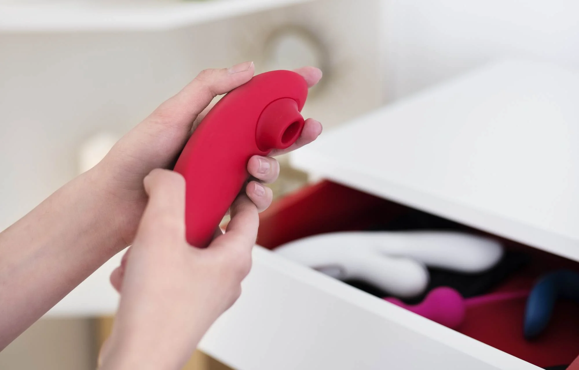 womanizer | Venclíkovi.cz Detail ženských rukou držících moderní diskrétní erotickou pomůcku u otevřeného šuplíku v ložnici.