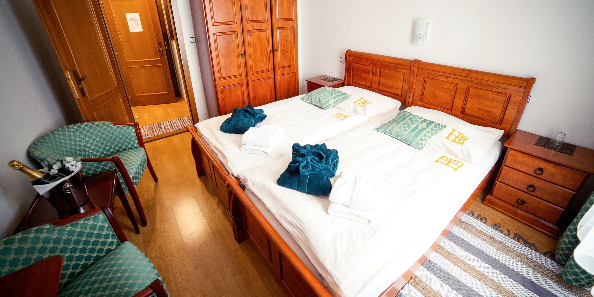 Dvoulůžkový pokoj s dřevěným nábytkem a zelenými křesly v hotelu Bristol