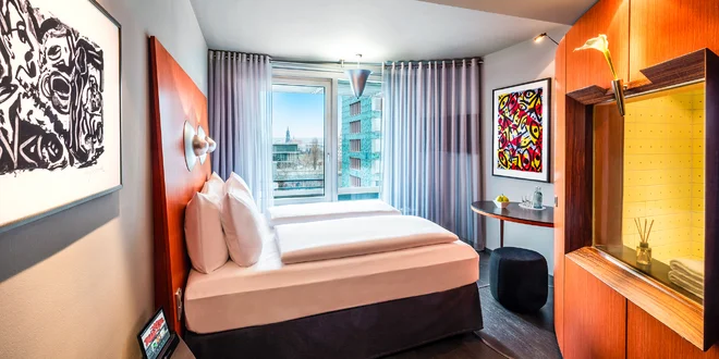 Dvoulůžkový pokoj Penck Hotelu s obrazy na stěnách a červeným čelem postele
