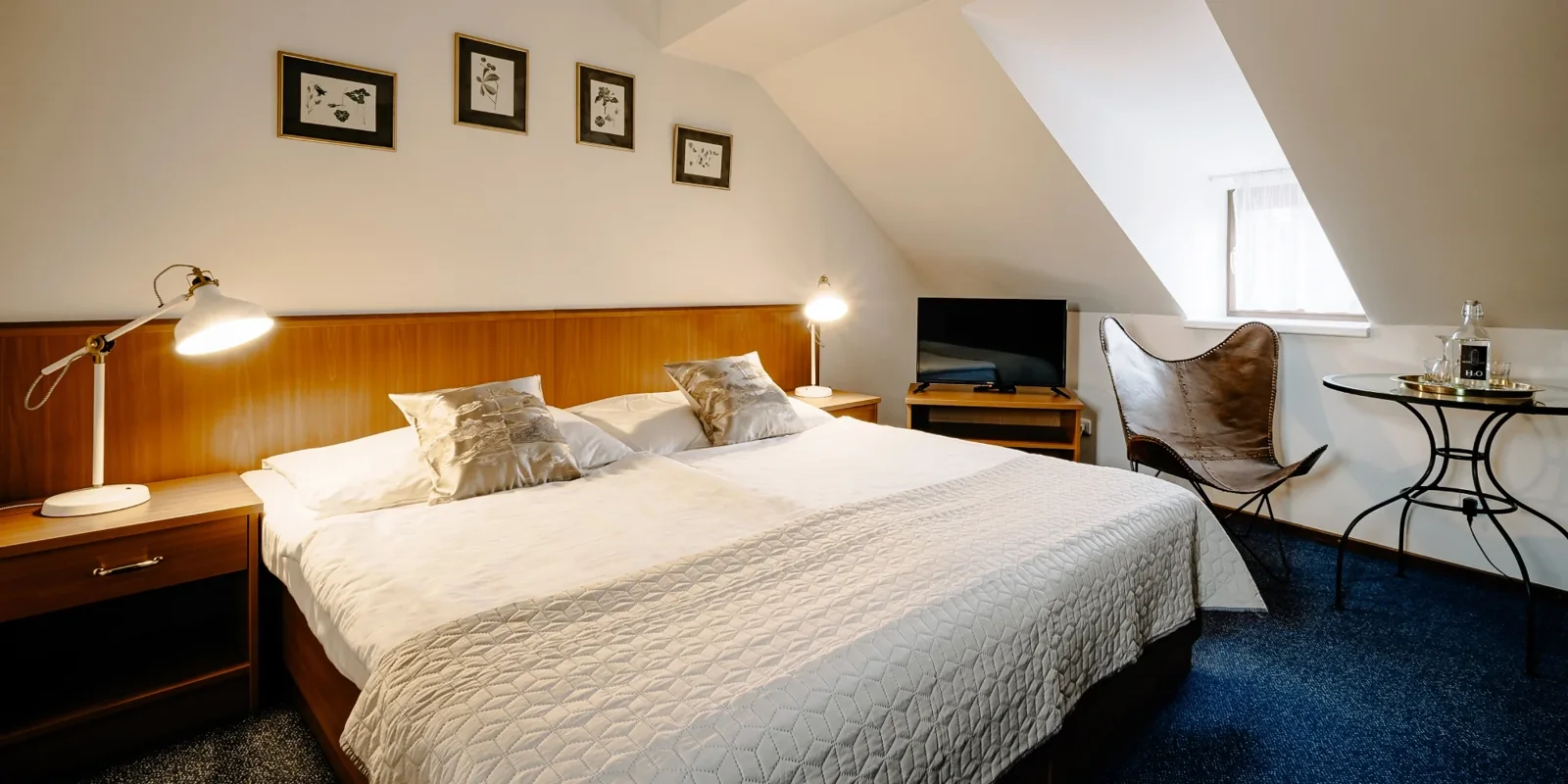 Podkrovní dvoulůžkový pokoj s bílým povlečením a modrým kobercem v Hotelu Galerie Třeboň