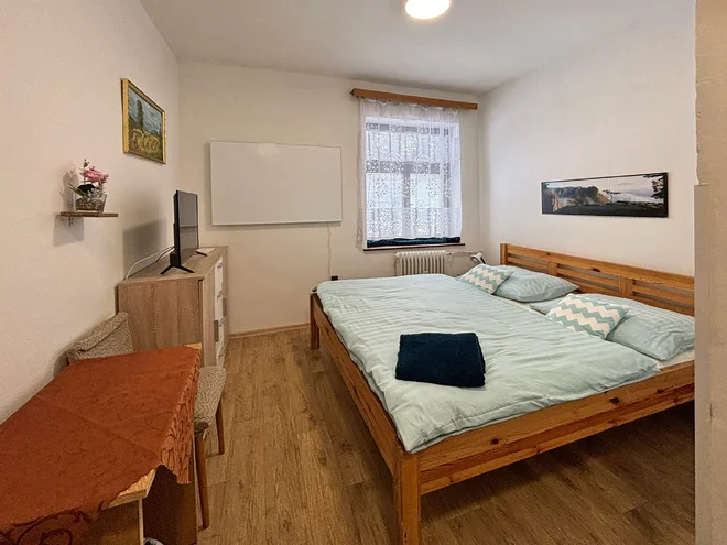 Pokoj hotelu JEF s dřevěnou dvoulůžkovou postelí a světlým povlečením