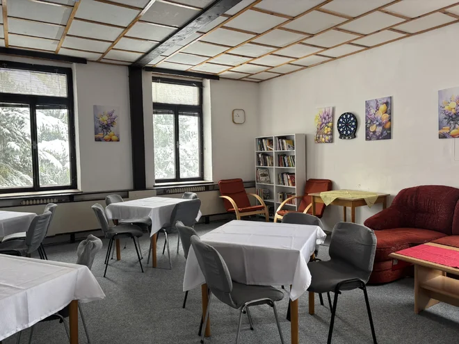 Společenská místnost hotelu JEF se stoly, křesly, knihovnou a šipkami
