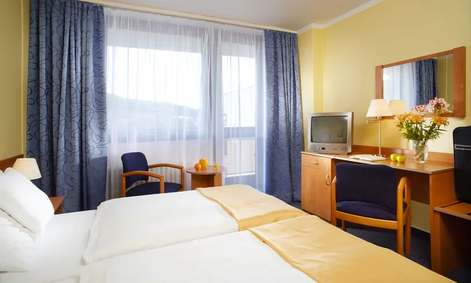 Dvoulůžkový pokoj hotelu Harmonie s modrými závěsy a žlutými stěnami