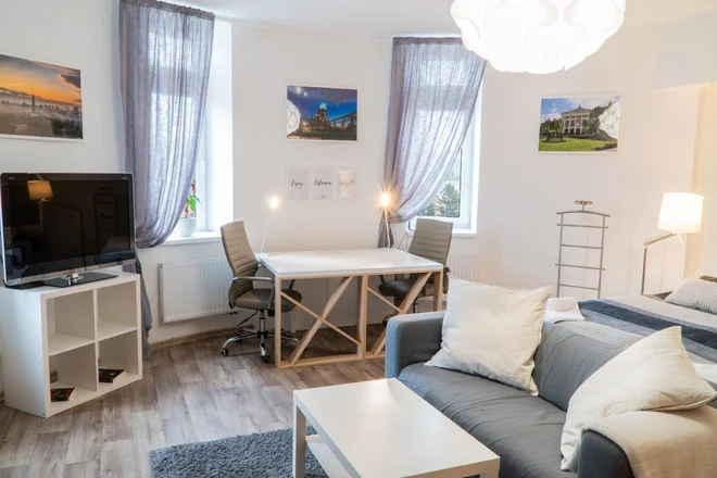 Světlý pokoj Kampus Palace s postelí, šedou pohovkou a jídelním stolem