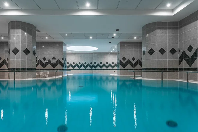 Vnitřní bazén hotelu Radium Palace s šedým obkladem a nerezovým zábradlím