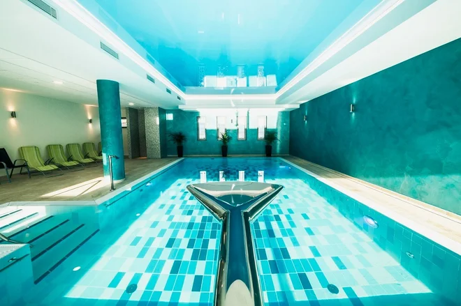 Vnitřní bazén hotelu Panorama s tyrkysovými stěnami, vodní atrakcí a lehátky