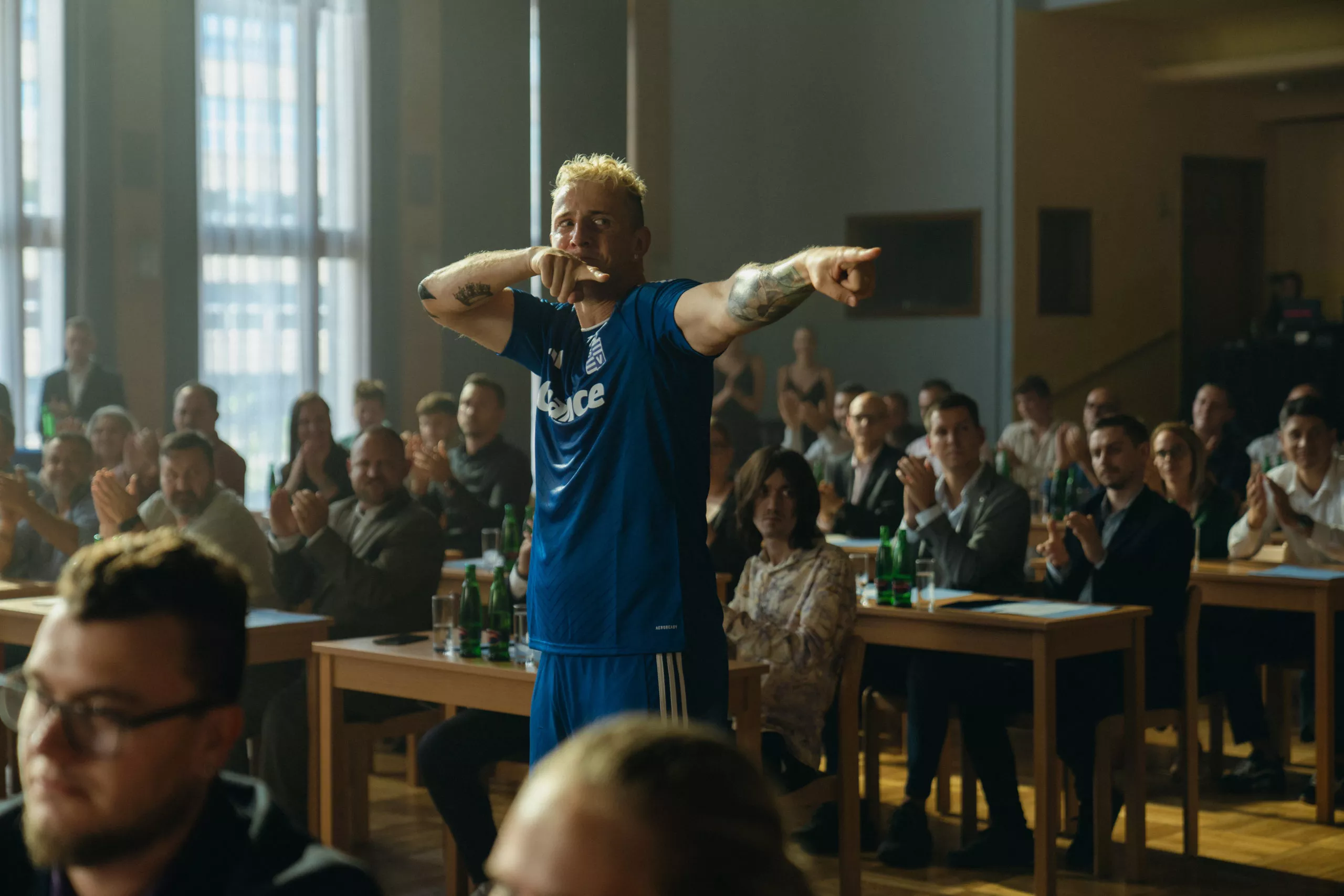 Lavi ve filmu Vyšehrad Dvje stojí před plným sálem, ukazuje prstem a působí sebejistě, hlasitě a teatrálně, přesně v duchu své přehnané fotbalové image