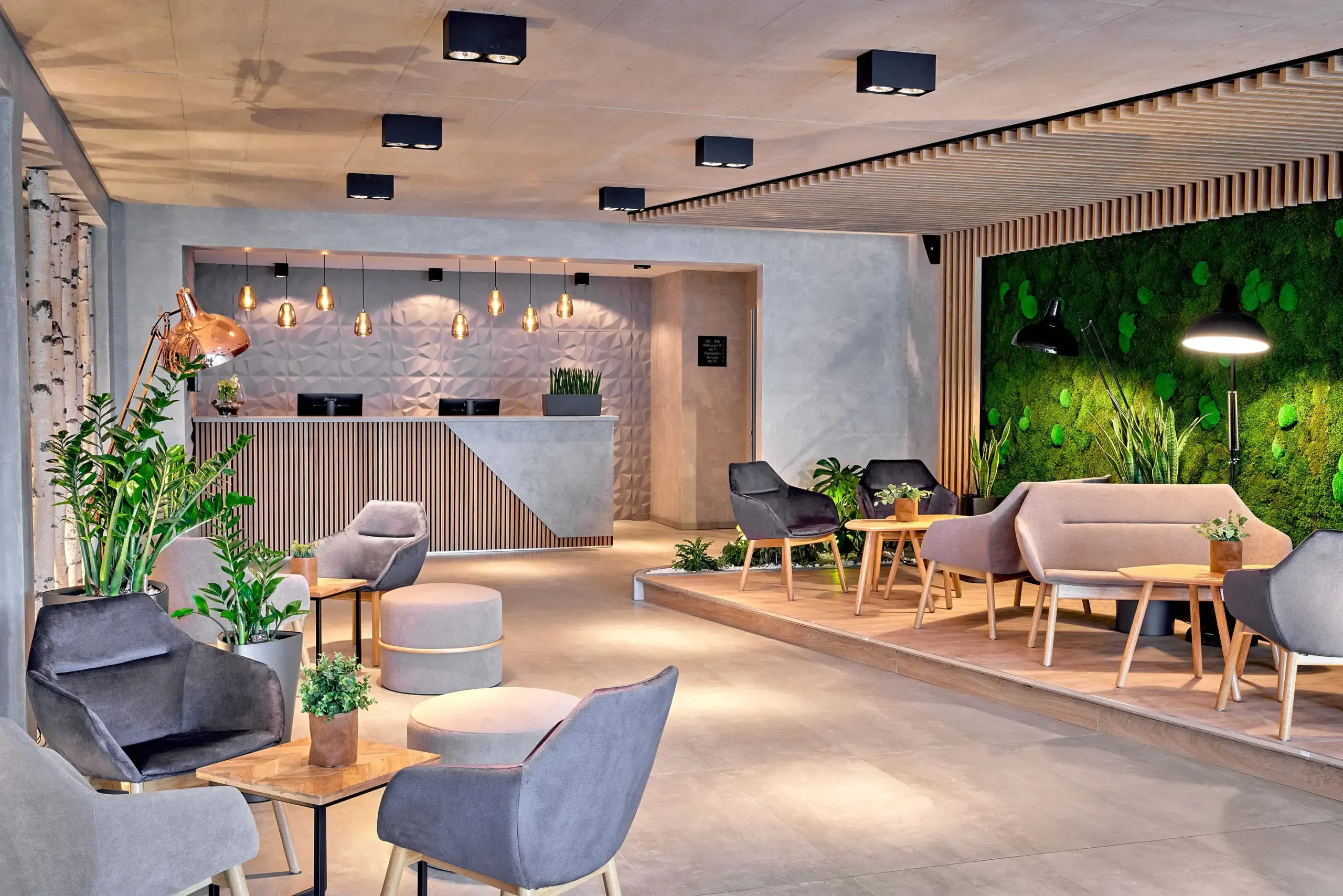 Recepce hotelu ever.grün Kaprun s pohodlným posezením, zelenou stěnou z mechu a útulným moderním interiérem.