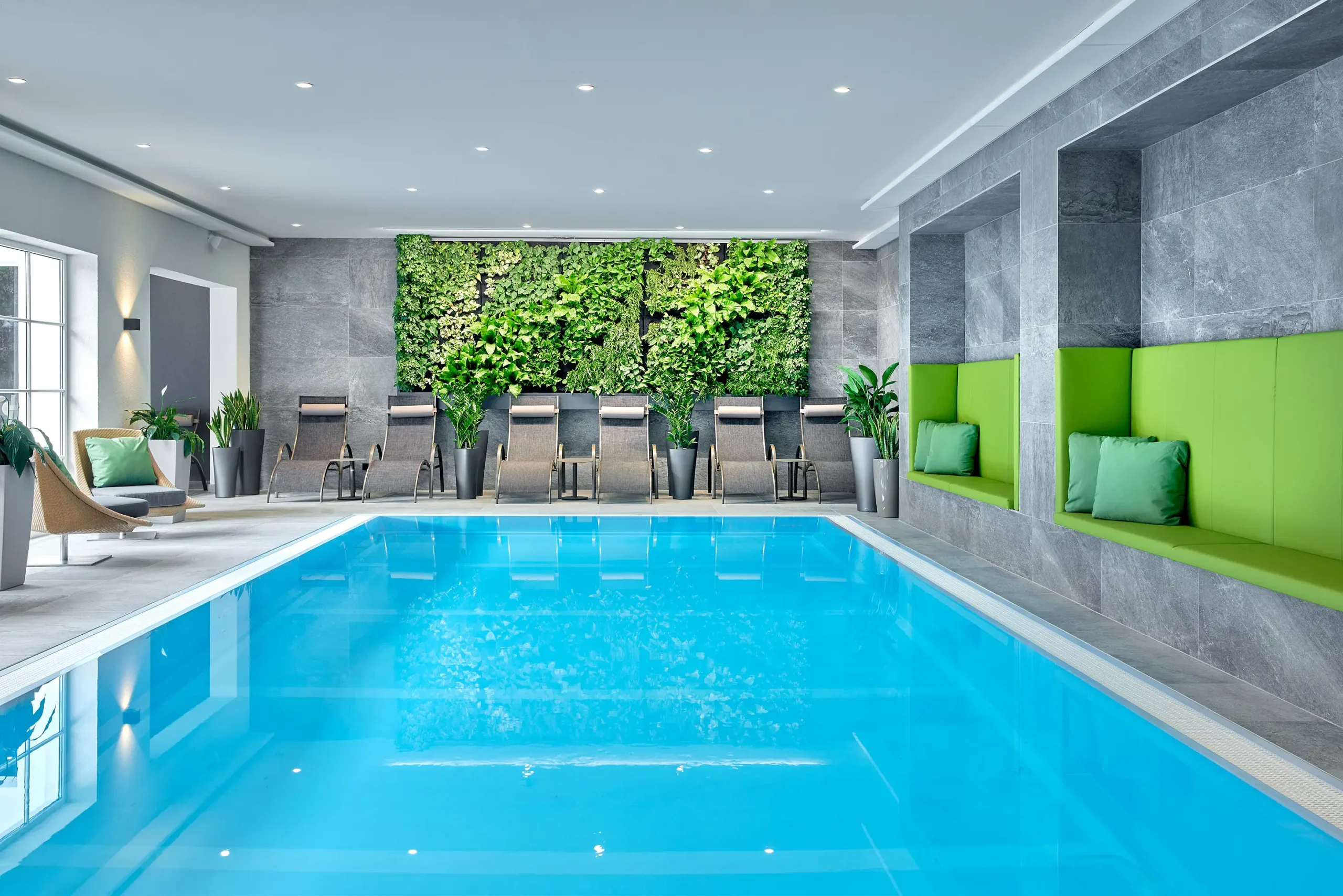Moderní wellness hotelu ever.grün Kaprun s modrým bazénem, zelenými rostlinami a pohodlnými lehátky v elegantním prostředí.